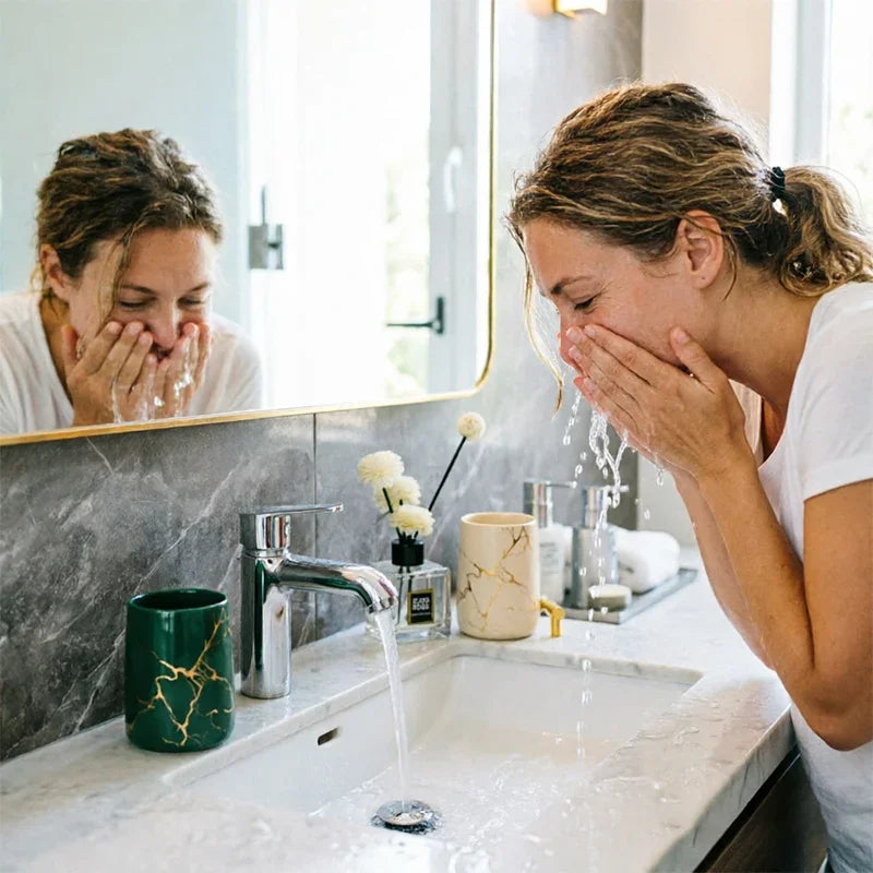 Woman washing her face at a marble sink with eprolo luxury ceramic bathroom tumblers.
