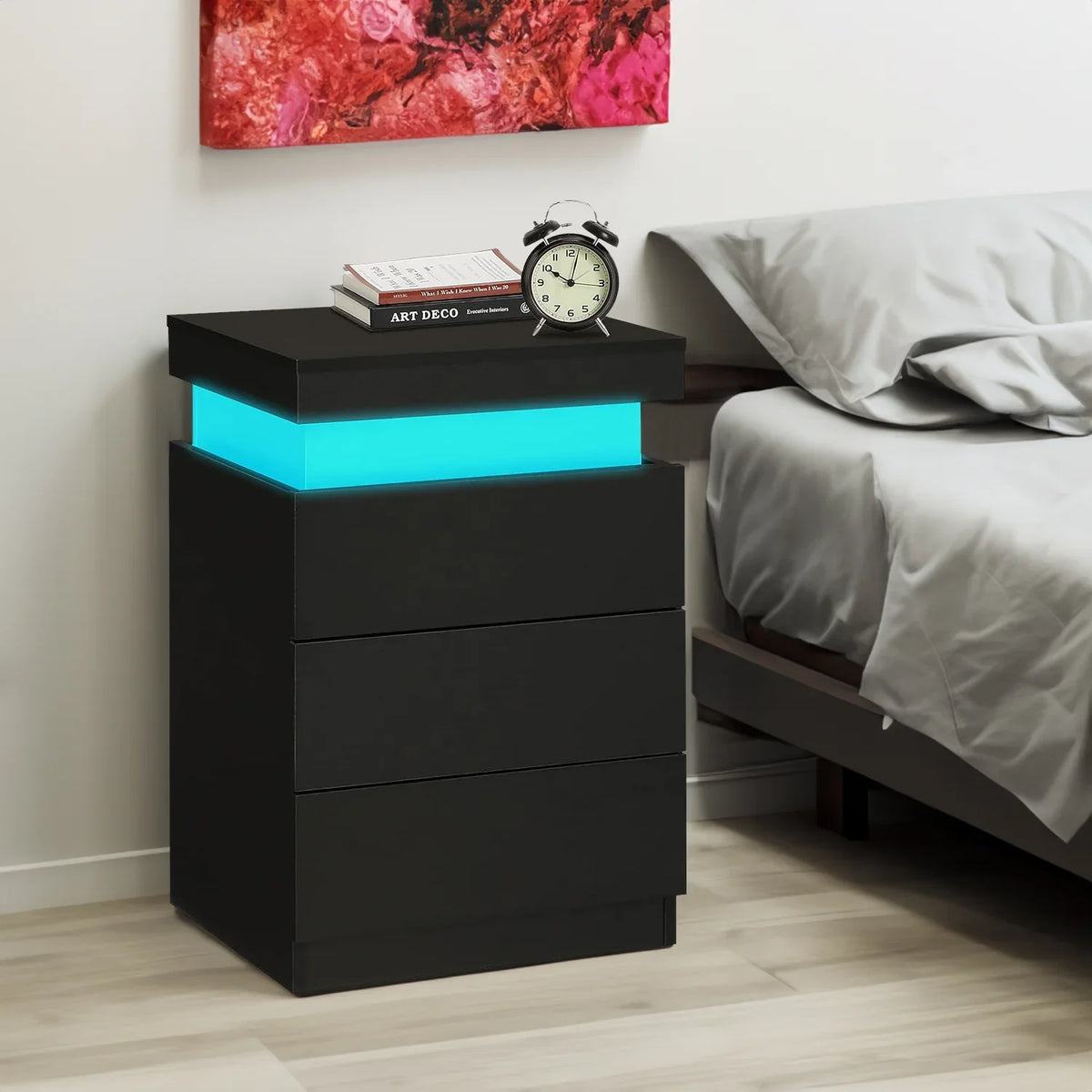 Modern black eprolo LED nightstand with blue light accent and books on top by a bed.