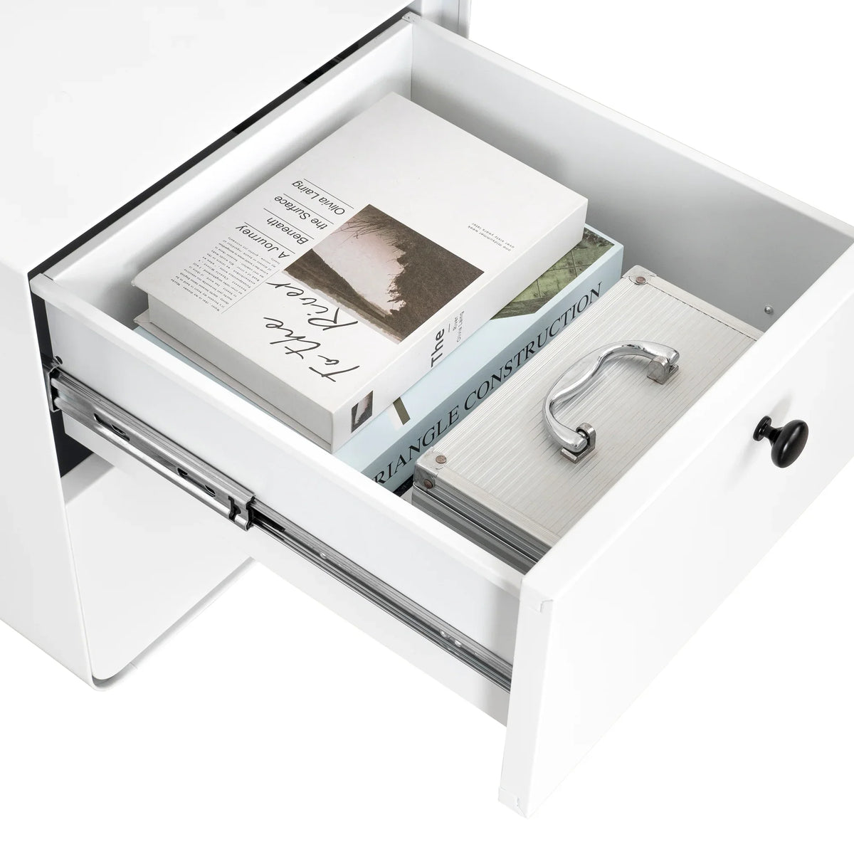Open drawer of an eprolo white steel night stand containing books and a silver organizer.
