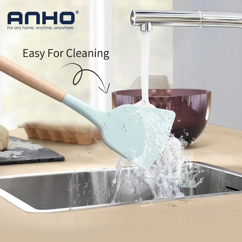 Light blue silicone spatula with wooden handle being washed under a running kitchen faucet.