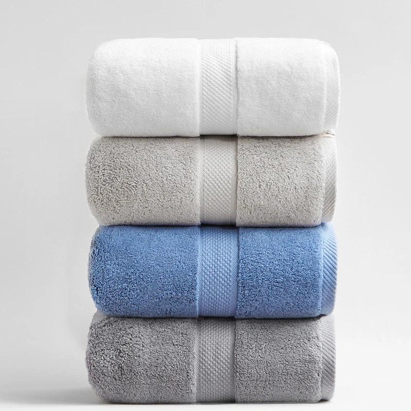 Stack of four luxury eprolo 100% cotton bath towels in white, beige, blue, and grey.