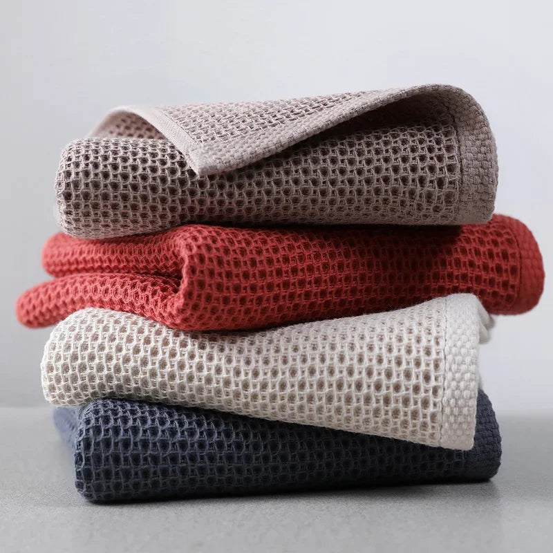 A stack of eprolo cotton waffle weave hand towels in beige, red, cream, and navy blue.